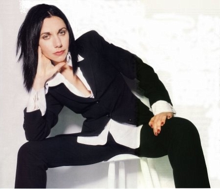 PJ Harvey im Anzug. lässig auf einem weißen Hocker sitzend